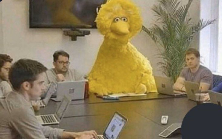 Der große gelbe Vogel aus der Sesamstrasse sitzt sitzt still am Konferenztisch zwischen mehreren Männern die scheinbar konzentriert auf ihre Laptops tippen, ohne ihn zu beachten.